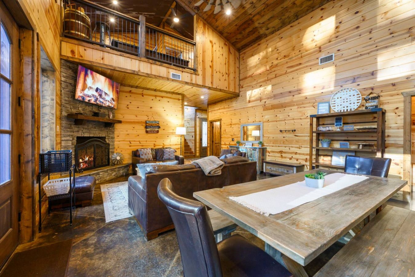 This cozy log cabin living space features a stone fireplace, leather seating, and a perfect spot to gather around the wooden table.