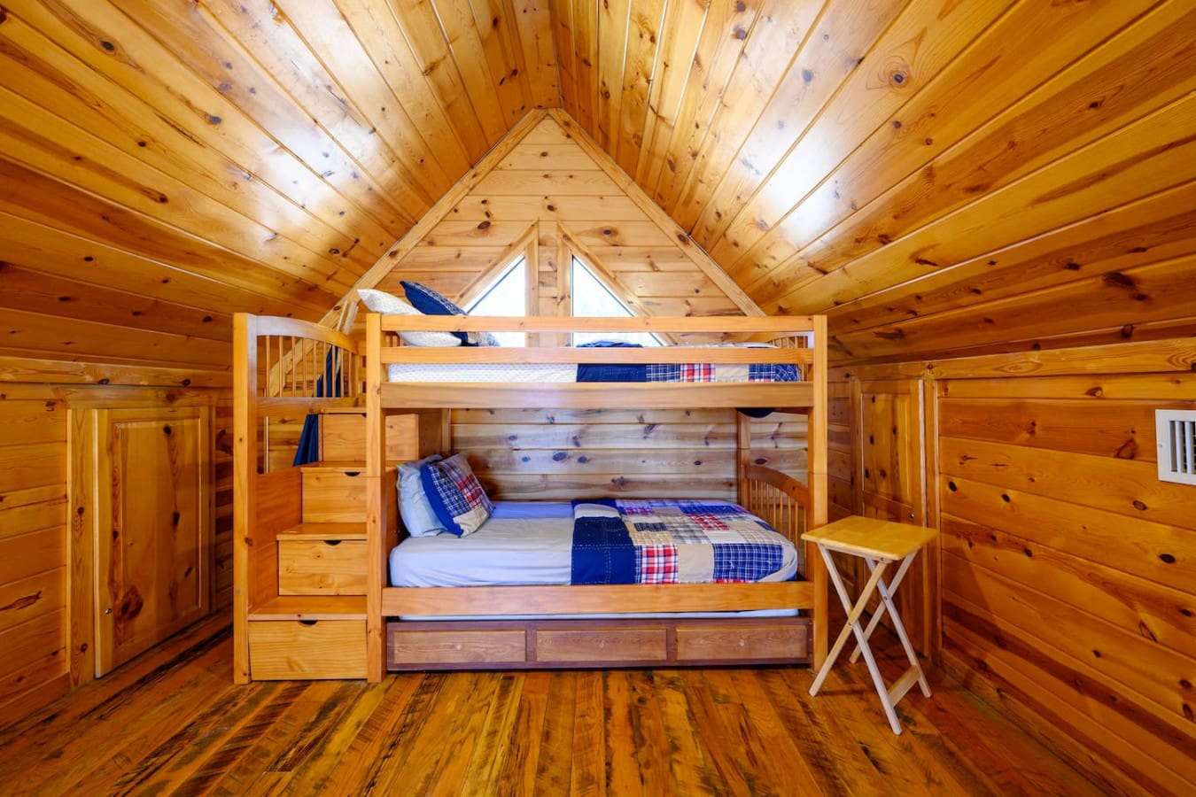 Cozy wood cabin bedroom with built-in bunk beds and plenty of natural light from the peaked ceiling windows.