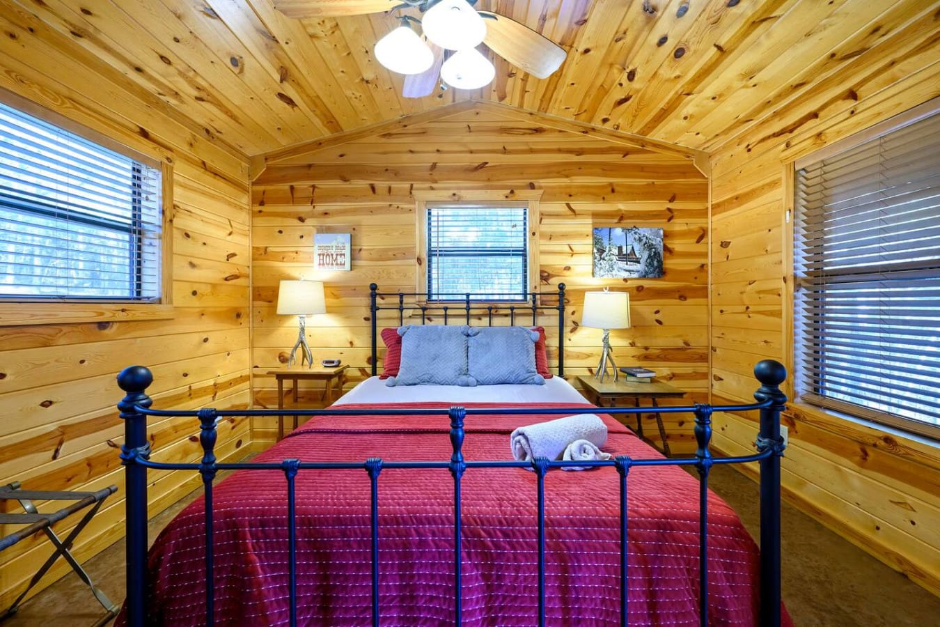 This cozy log cabin bedroom features a charming wrought iron bed with plenty of natural light and wood-beamed charm.