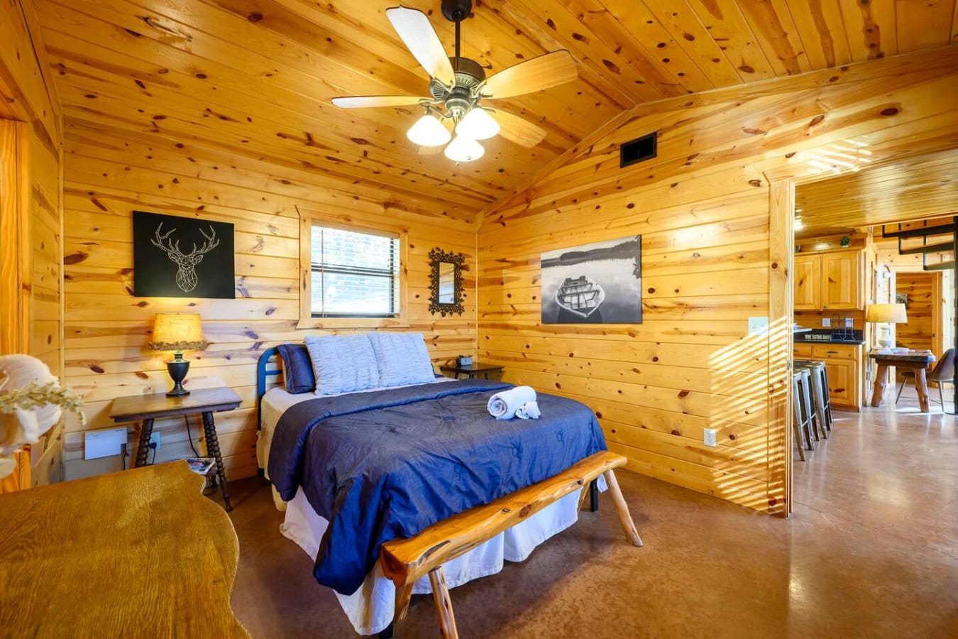 Cozy knotty pine cabin bedroom with a comfy bed, ceiling fan, and plenty of natural light from the windows.