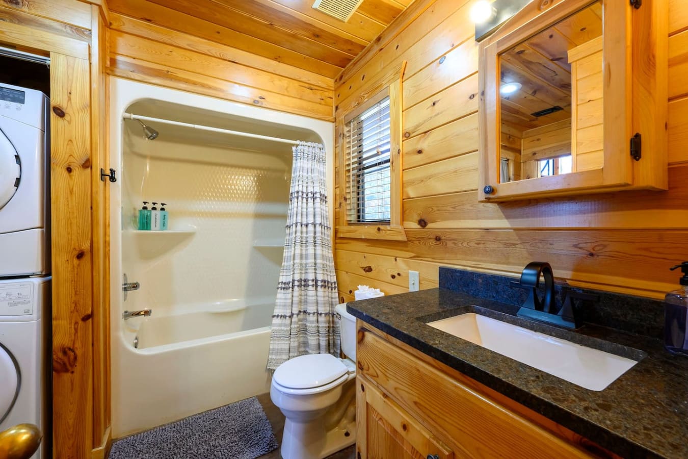 This cozy bathroom features warm wood paneling, granite countertops, and a full shower-tub combo.
