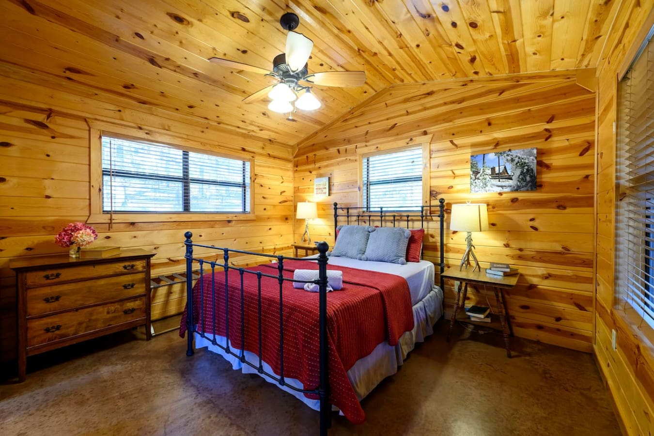 This cozy log cabin bedroom features a wrought iron bed, warm pine walls, and plenty of natural light from the windows.
