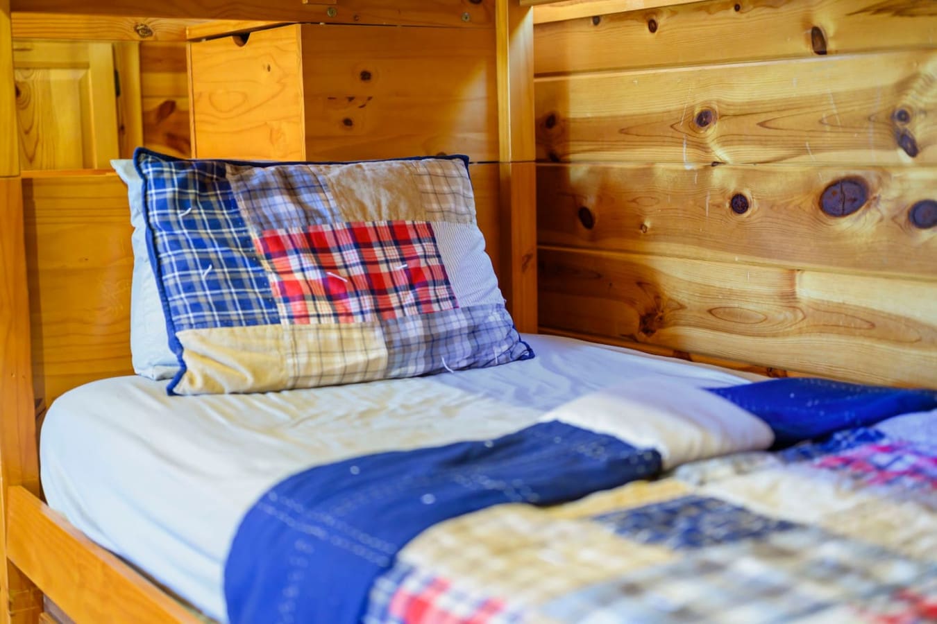 Cozy wooden cabin bedroom with crisp blue and plaid bedding perfect for a restful mountain getaway.