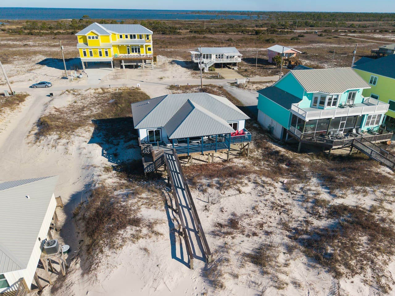 Colorful beachfront homes with elevated decks overlooking sandy dunes and water views in a quiet coastal community.