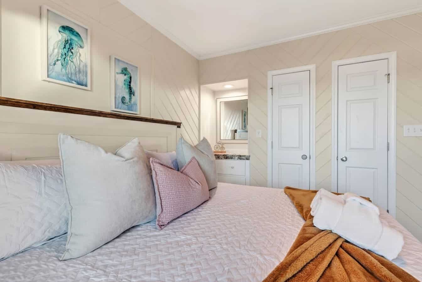 This serene coastal bedroom features crisp linens, ocean-inspired art, and plenty of natural light streaming through those gorgeous windows.