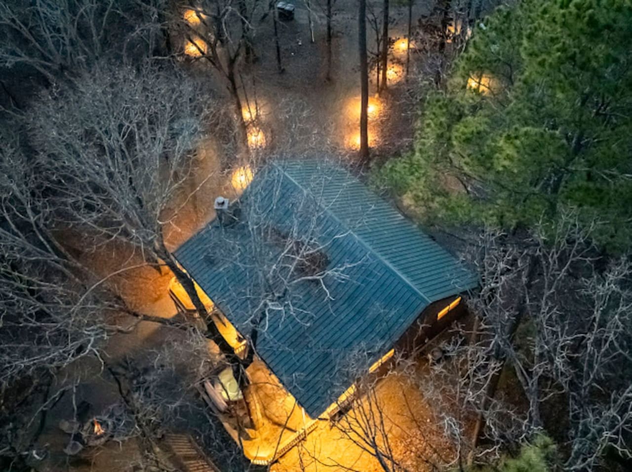 Cozy cabin nestled in the woods with warm lighting and a peaceful deck overlooking the trees at dusk.