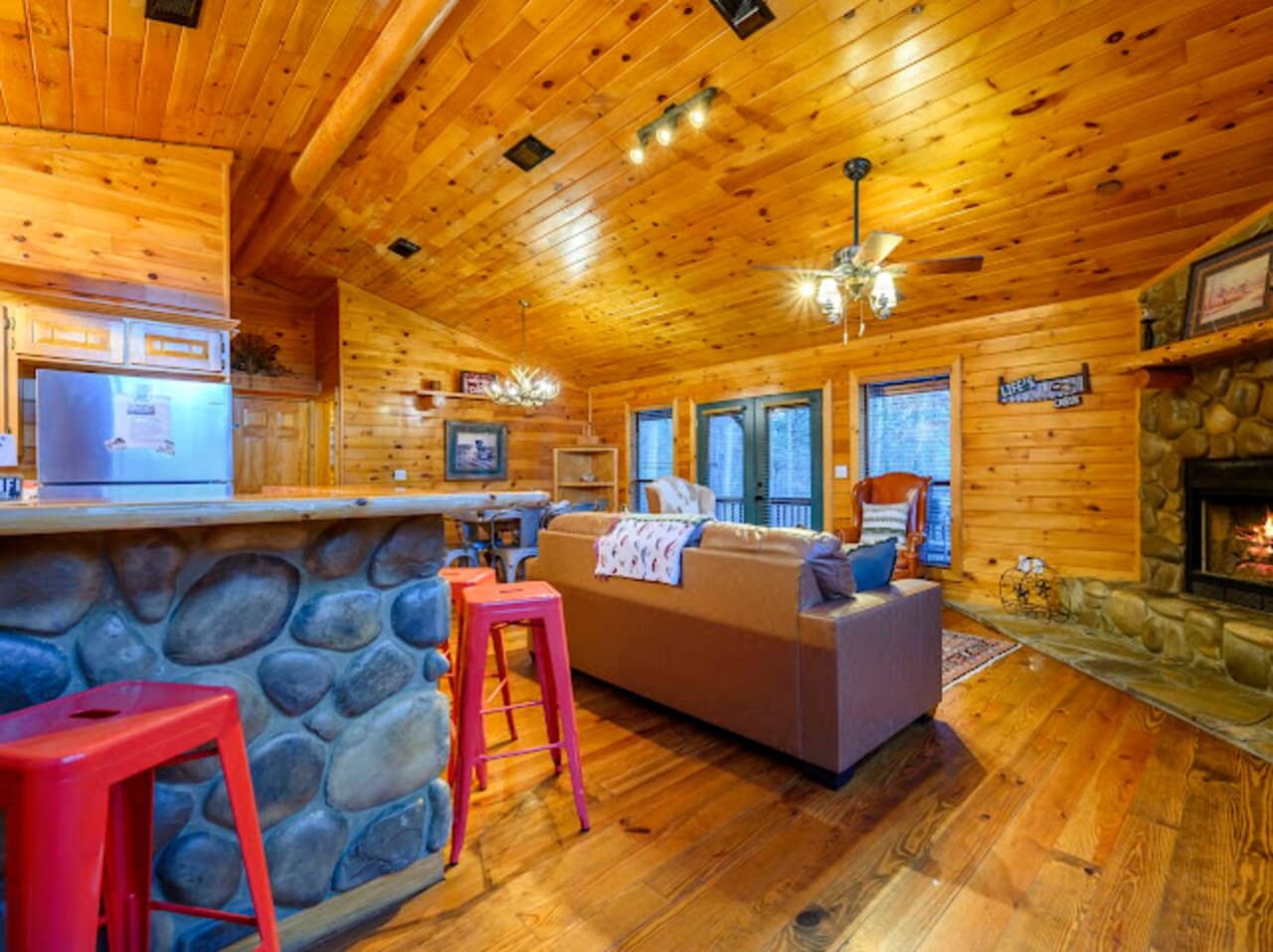 This open-concept cabin is all golden wood, stone fireplace vibes, and packed with cozy seating areas perfect for gathering.