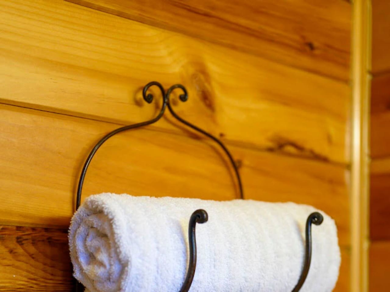 Rustic wooden walls and charming wrought-iron towel holder bring cozy elegance to every bathroom corner.