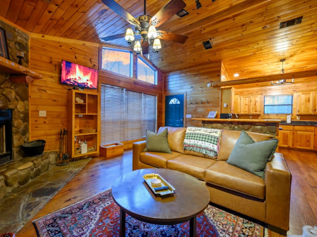 This cozy cabin living room features wood beams, a stone fireplace, and plenty of natural light from the windows.