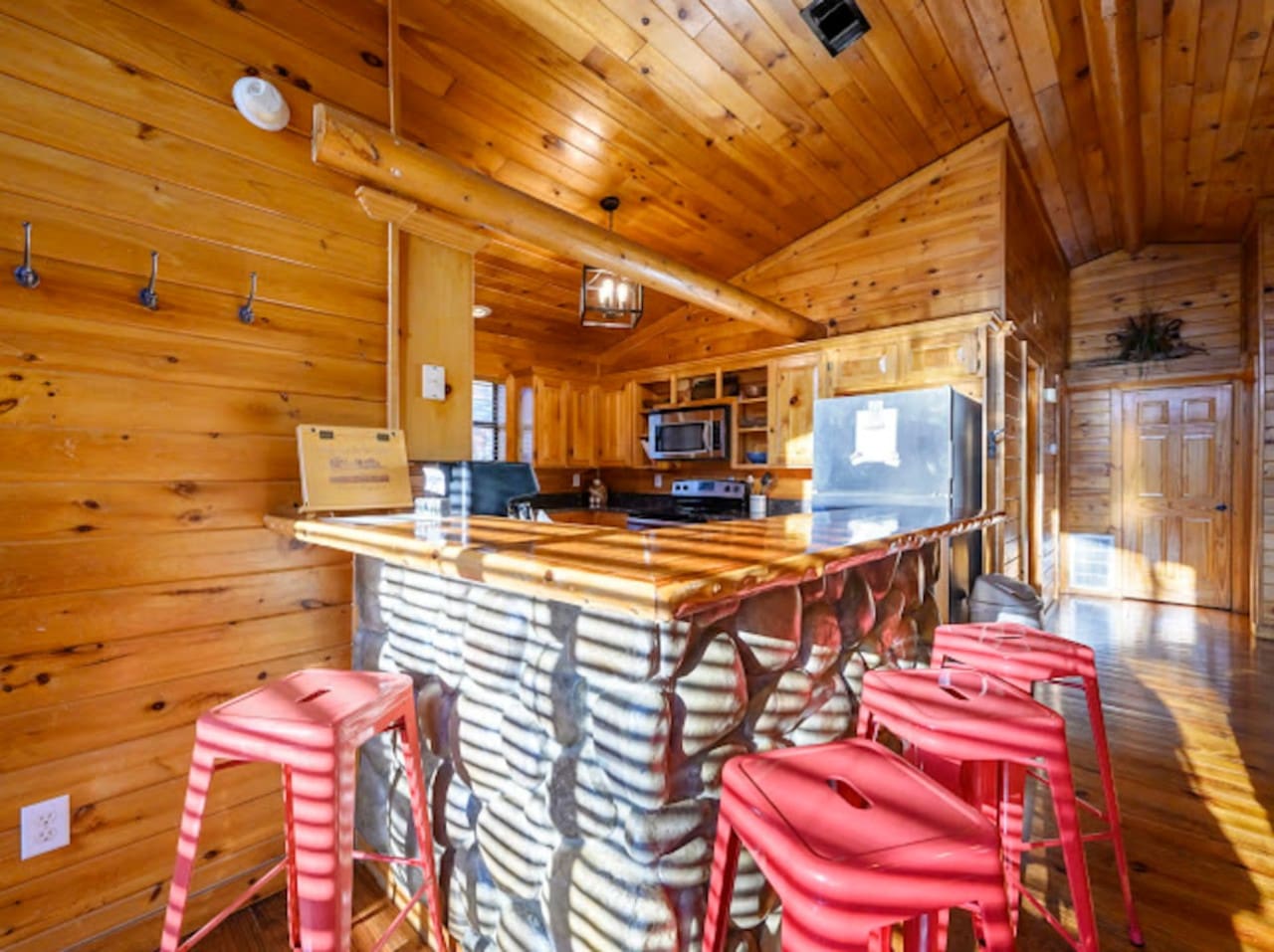 This gorgeous log cabin kitchen features a stunning island with red stools and opens to beautiful views through the glass doors.