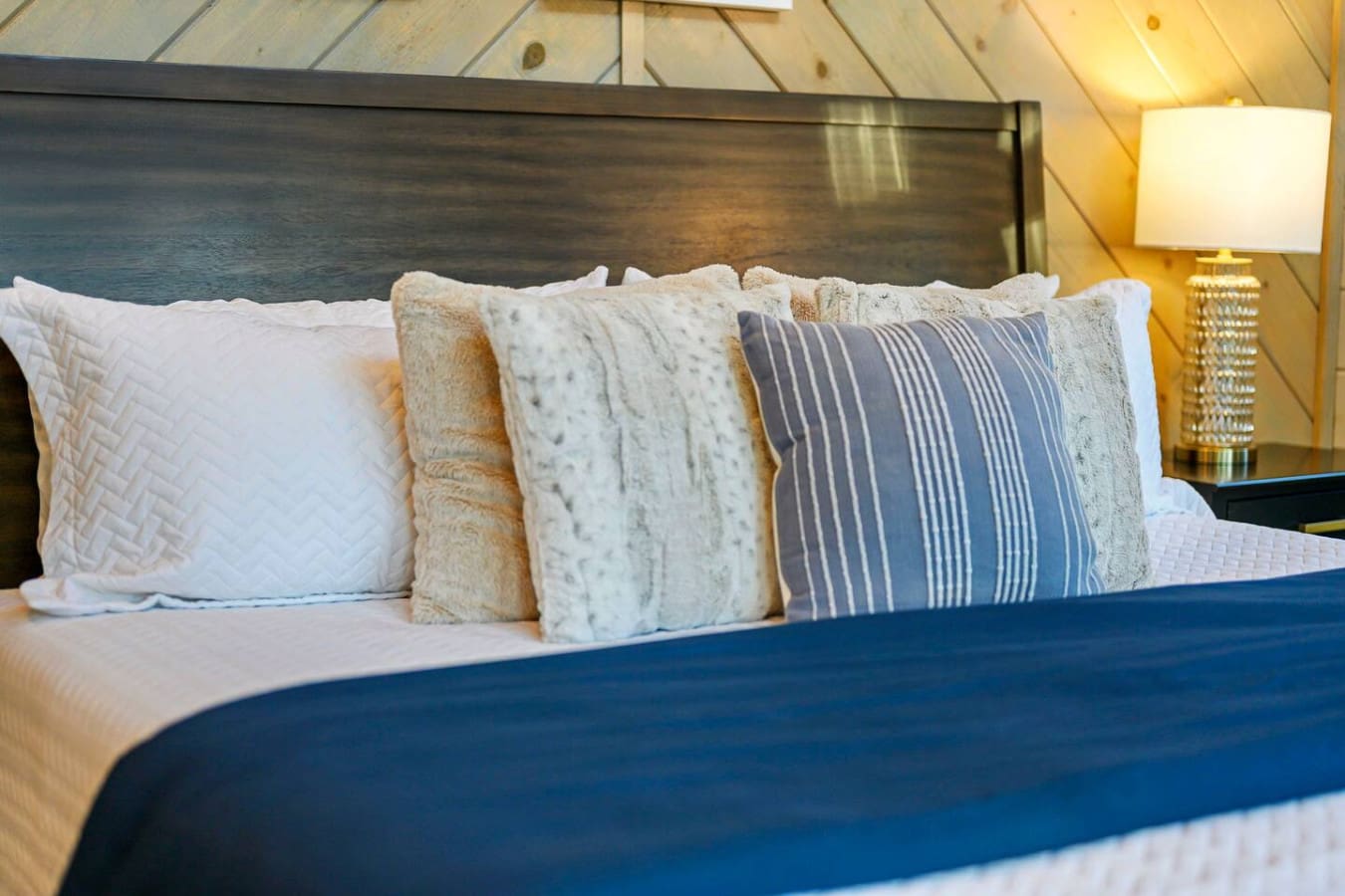 This cozy bedroom features a beautiful dark wood headboard and layers of soft, textured pillows perfect for a good night's sleep.