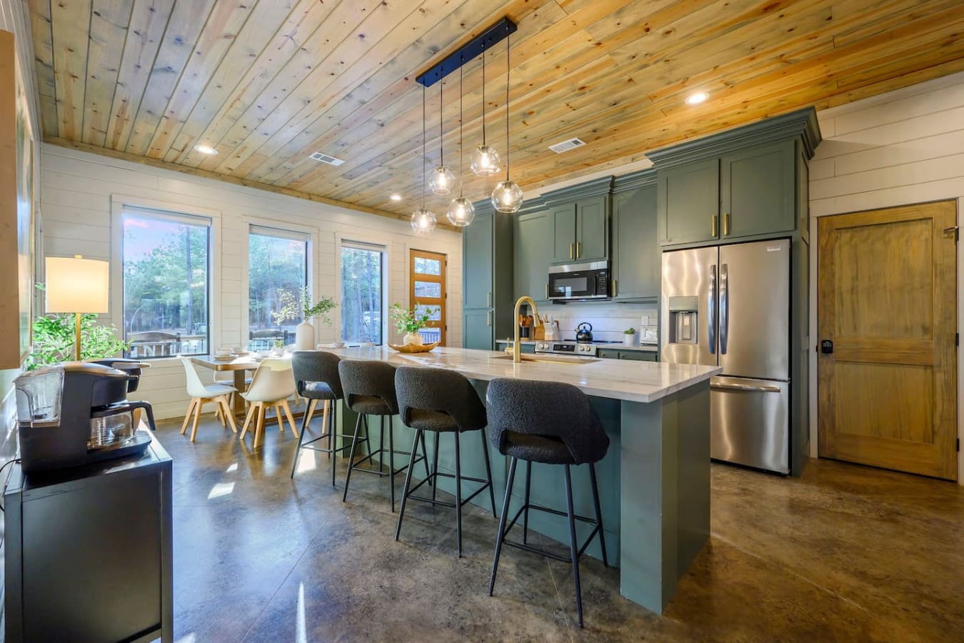 This kitchen is absolutely stunning with those forest views, wood ceilings, and tons of natural light pouring in.