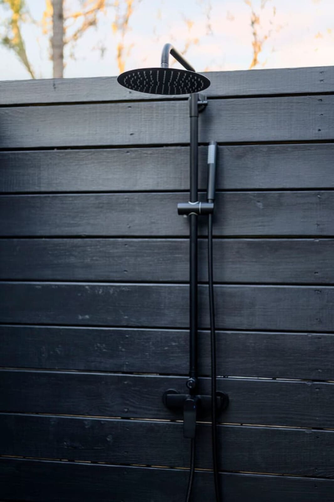 Nothing is coming to mind here - this is just an outdoor shower mounted on a black wooden wall with trees in the background.