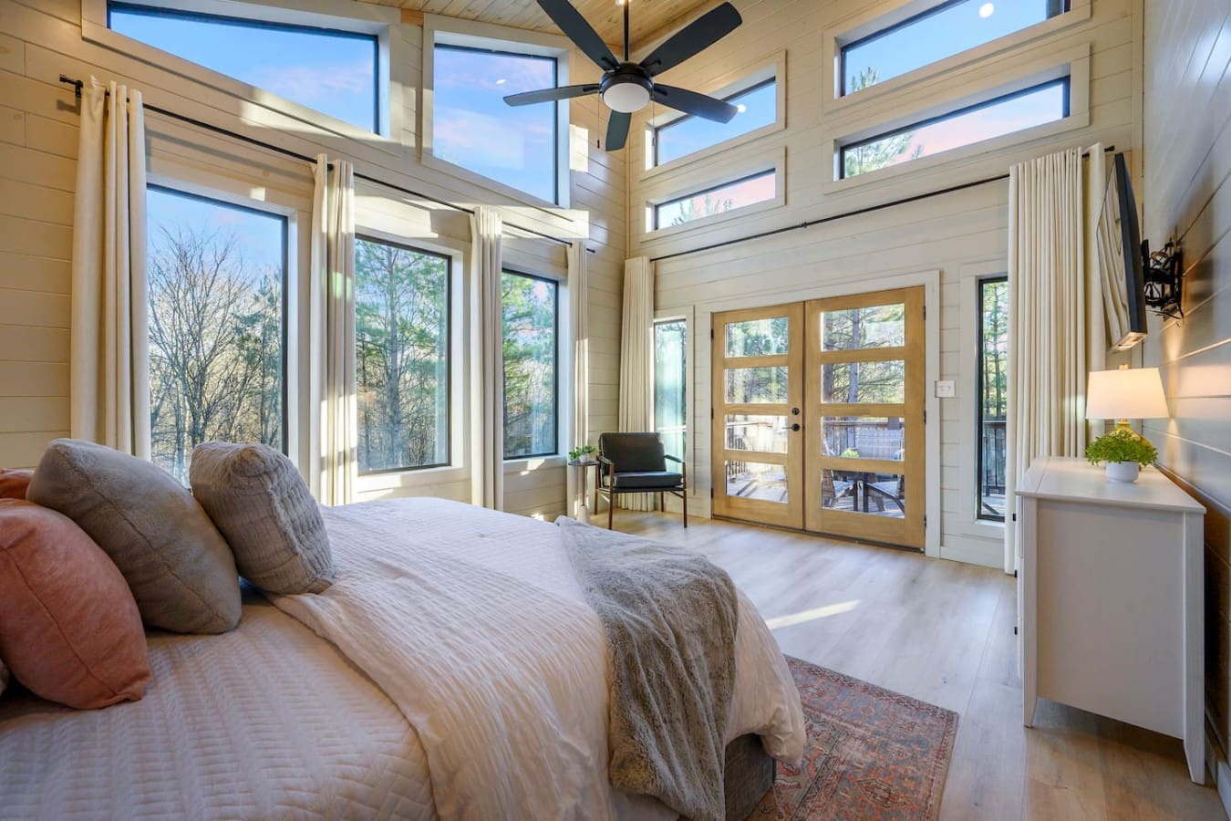 This bedroom is basically a glass box overlooking the forest with a ceiling fan and doors opening to a deck.