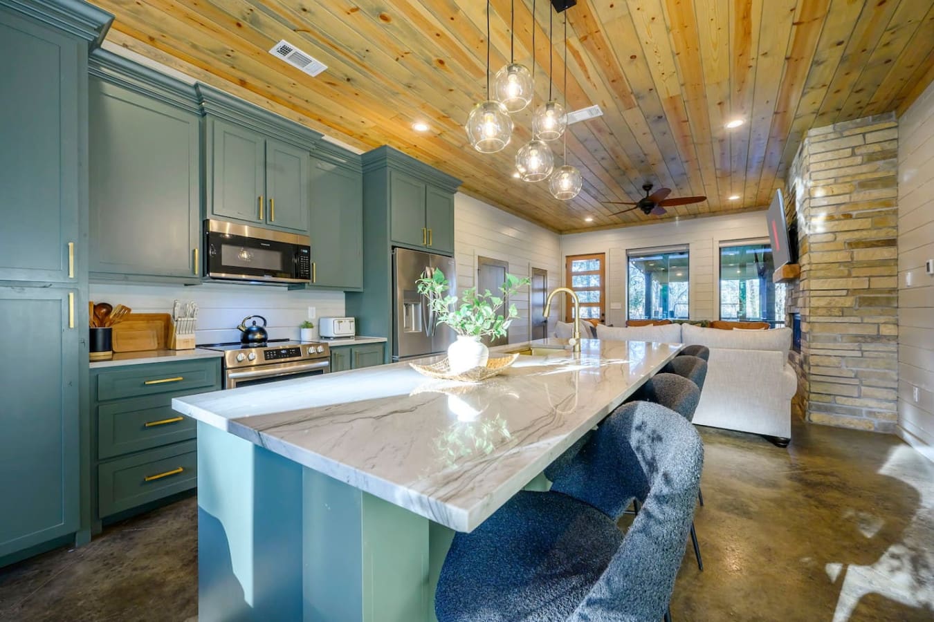 This modern kitchen features custom green cabinetry, marble countertops, and a gorgeous wood ceiling with pendant lighting.