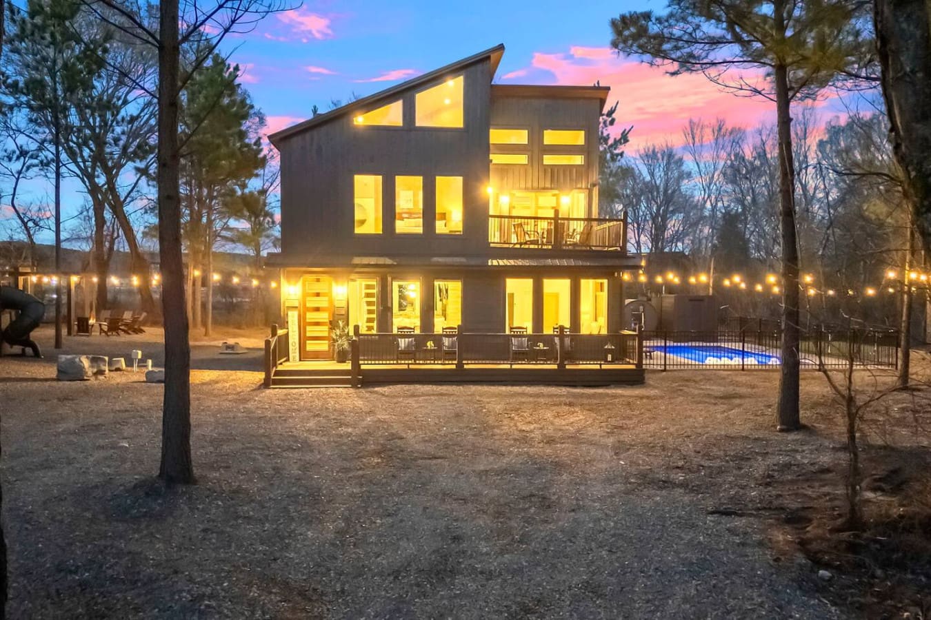 This stunning modern home glows against the twilight sky, nestled privately among the pines with a sparkling pool and spacious grounds.
