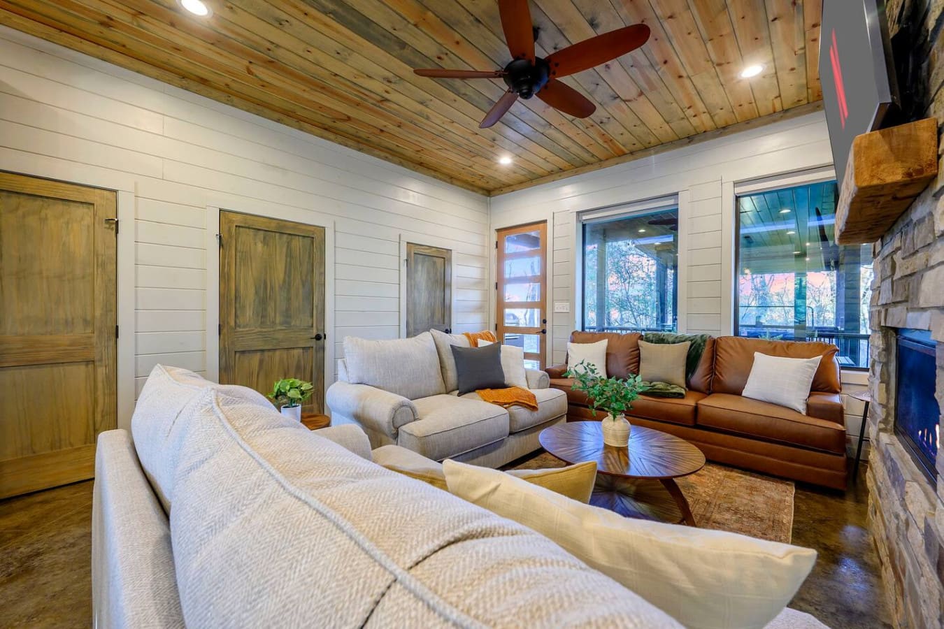 This stunning open-concept living room features floor-to-ceiling windows, a wood ceiling, and comfortable seating perfect for gathering.