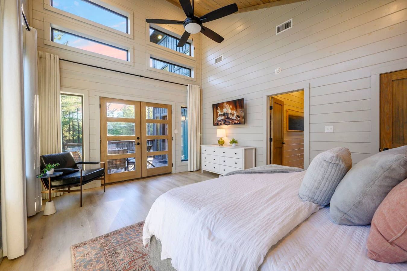 This spacious primary suite features floor-to-ceiling windows, a cozy sitting area, and direct deck access with stunning forest views.
