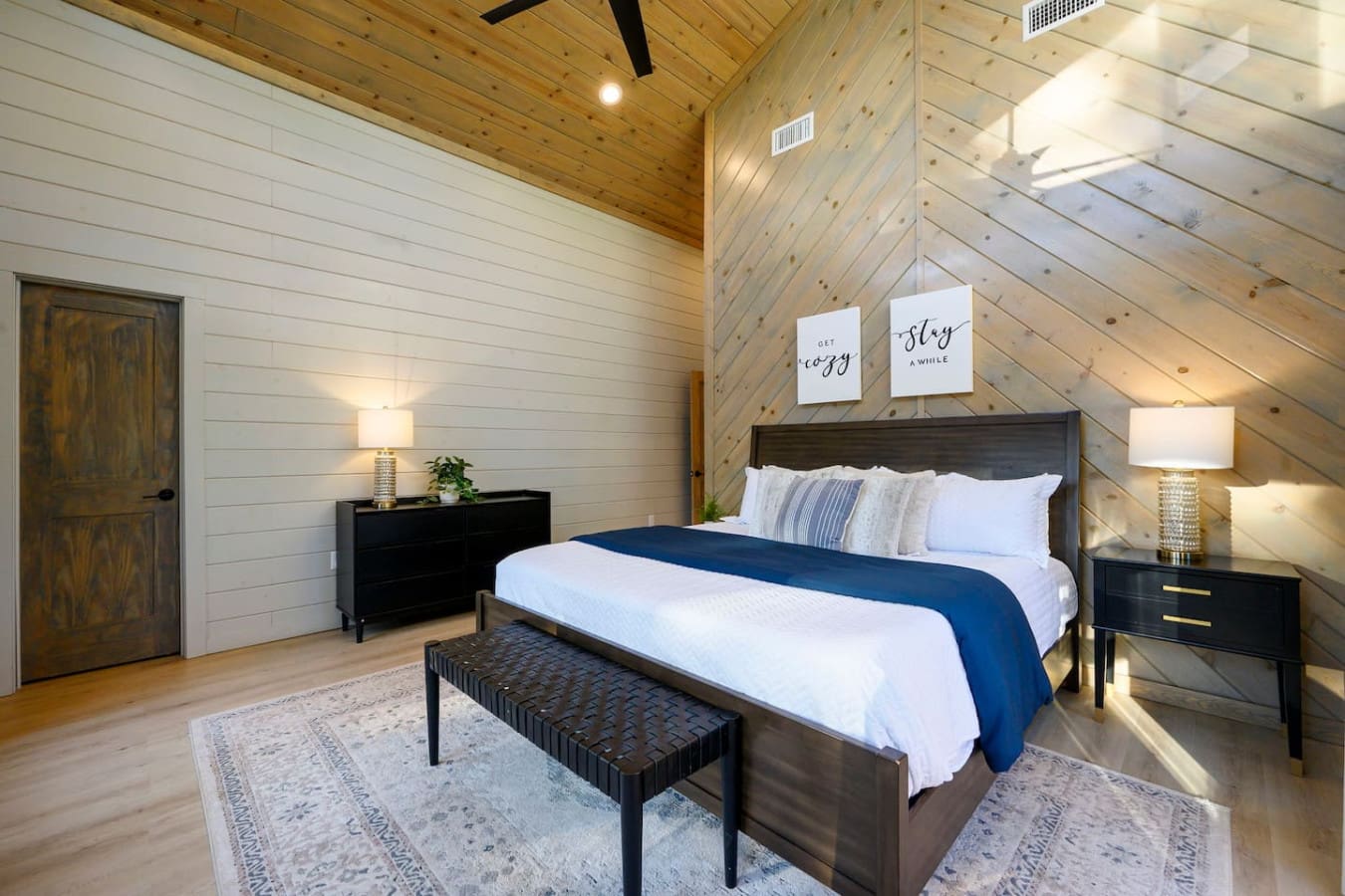 This cozy loft bedroom features vaulted wood ceilings, skylights, and a dark wood bed frame with luxury bedding.