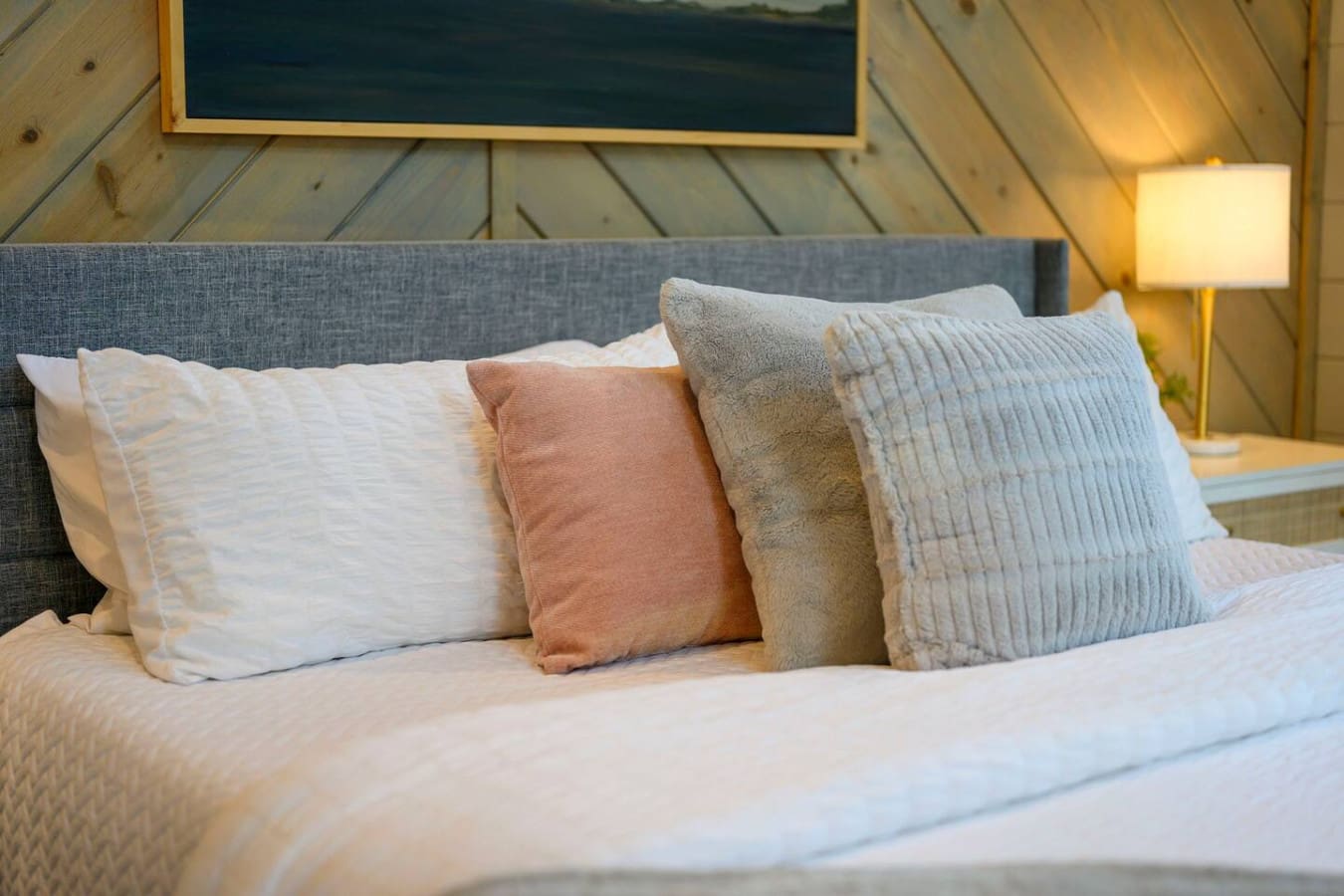 Cozy bed setup with layered pillows and a vaulted wooden ceiling that makes you never want to leave.