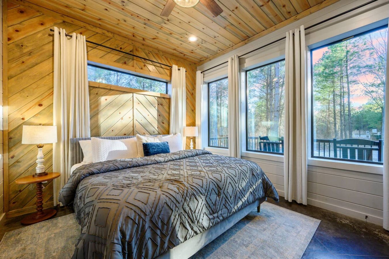 Wake up to forest views in this stunning bedroom with floor-to-ceiling windows and a cozy wood-beamed ceiling.