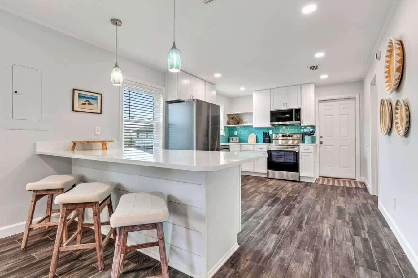 This gorgeous modern kitchen features stainless steel appliances, a spacious island with seating, and a stunning turquoise tile backsplash.