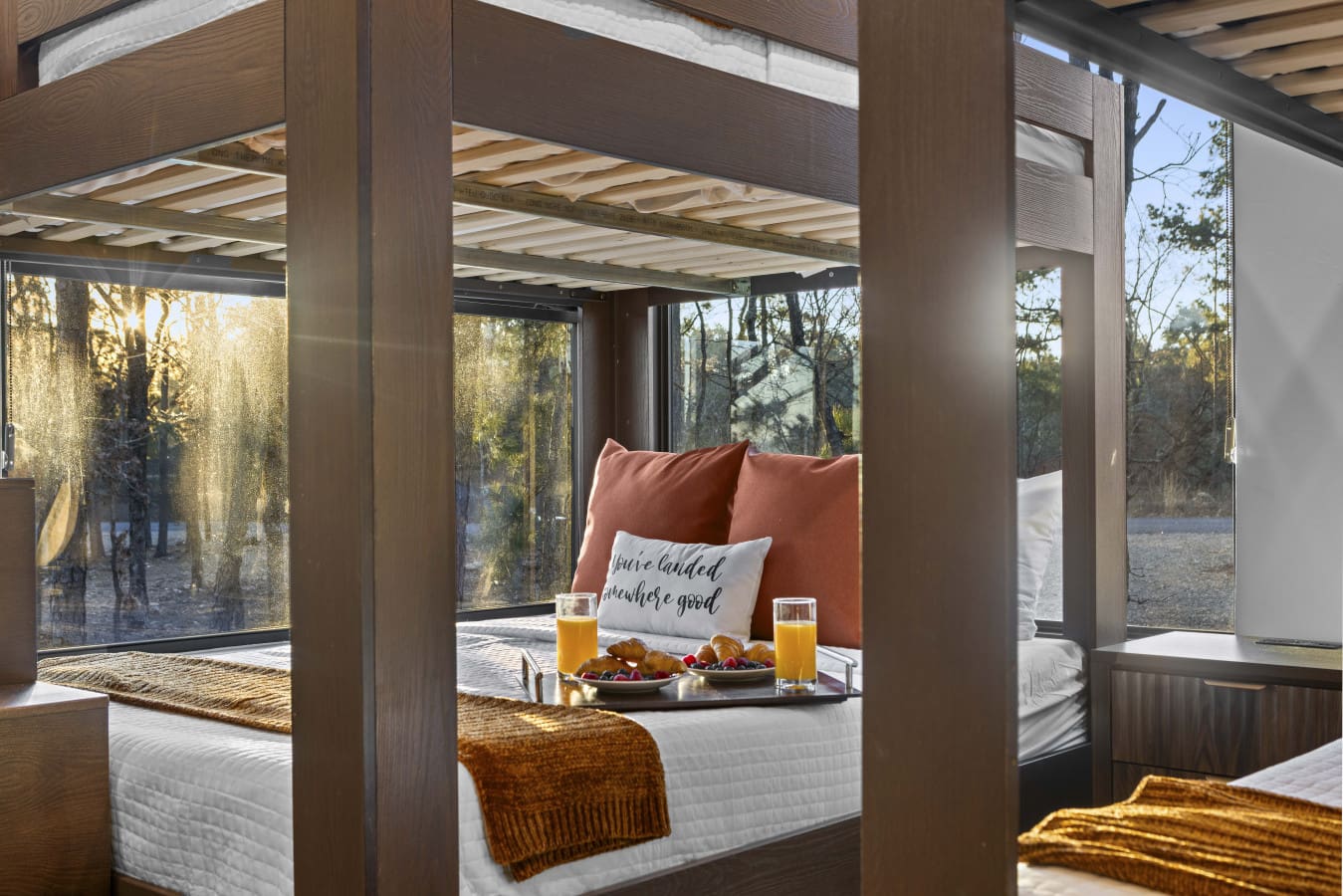 Floor-to-ceiling windows and golden morning light filtering through the trees — this bedroom wakes you up right.