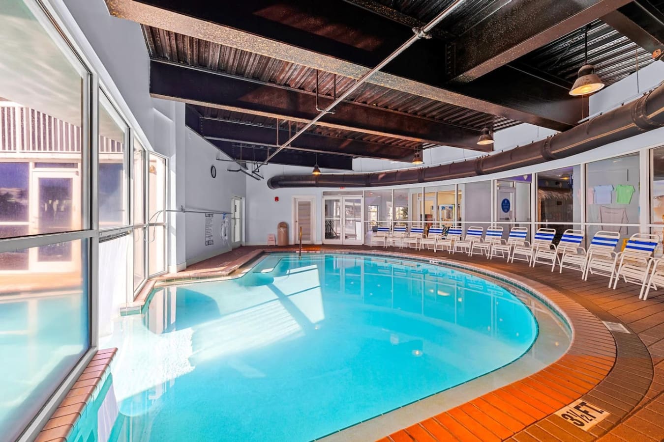 The indoor pool setup here is basically your rain-or-shine escape—loungers lined up, those industrial ceiling beams adding character, and enough natural light pouring through the windows to make you forget you're not outside.