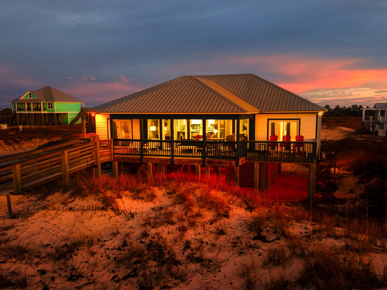 Golden hour glow hits this beachfront stunner with floor-to-wall windows and an elevated deck overlooking the dunes.