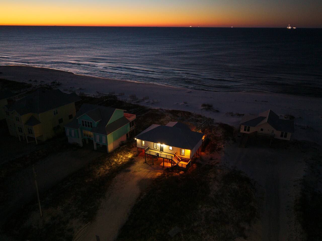 Beachfront home with lit interior glowing against the golden sunset over the ocean.