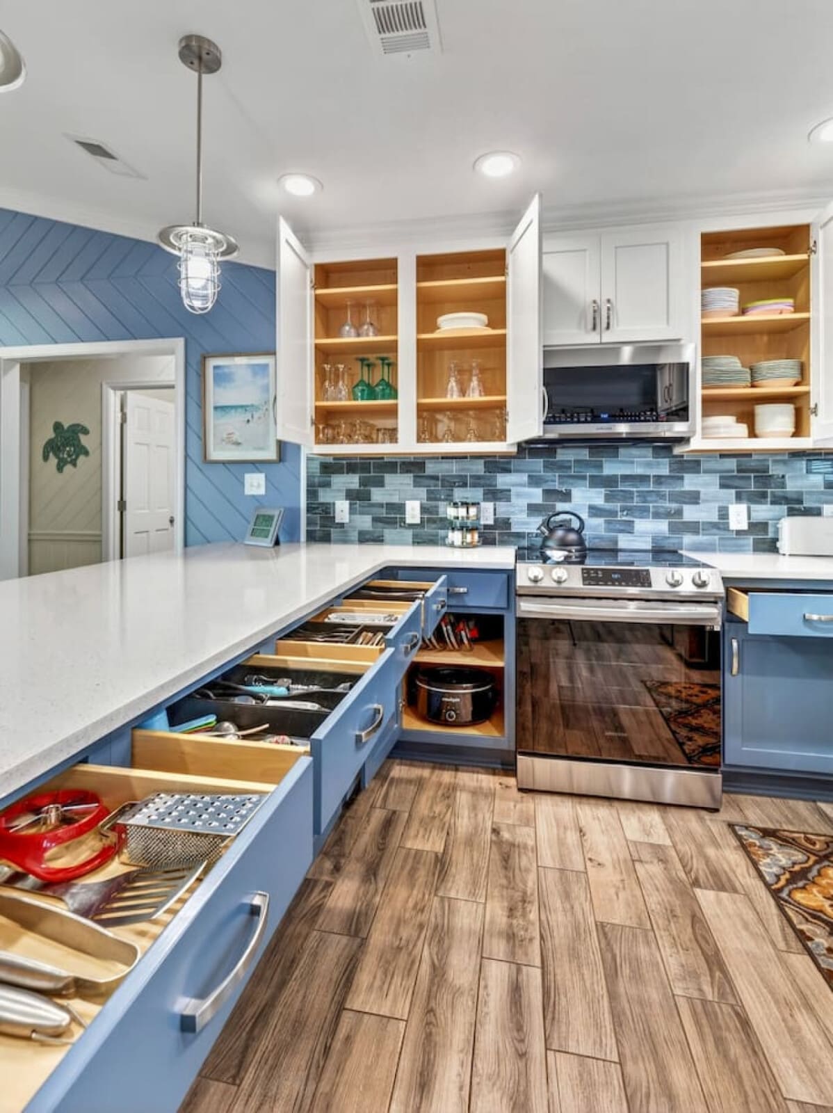 This gorgeous coastal-inspired kitchen features custom white and blue cabinetry with warm wood shelving and a stunning blue subway tile backsplash.