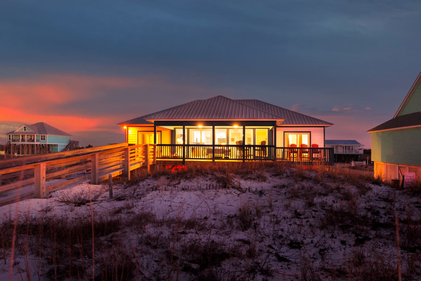 Stunning beachfront home glowing at sunset with wraparound deck and direct sand access.