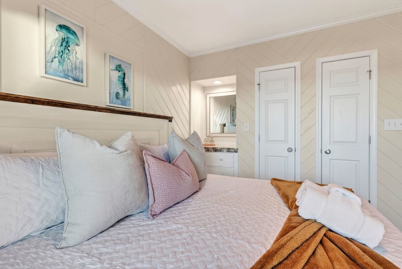This serene coastal bedroom features crisp linens, ocean-inspired art, and plenty of natural light streaming through those gorgeous windows.