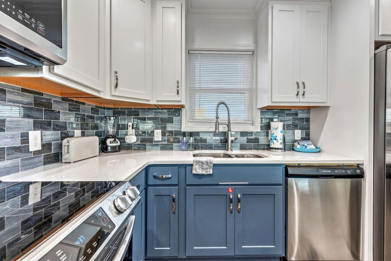 This sleek kitchen features crisp white upper cabinetry, navy blue base cabinets, and a beautiful tiled backsplash.
