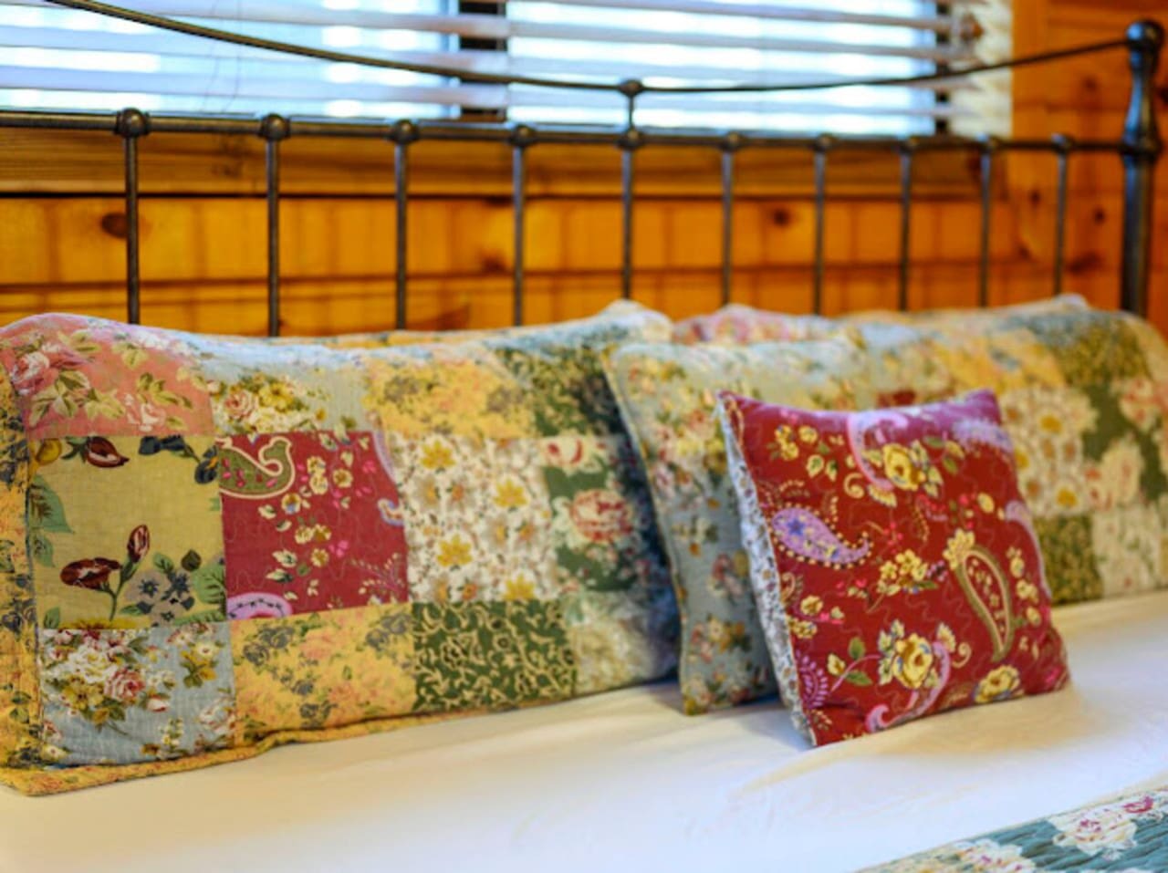 Cozy bedroom with a gorgeous wrought iron headboard and patchwork floral pillows that'll make you never want to leave.