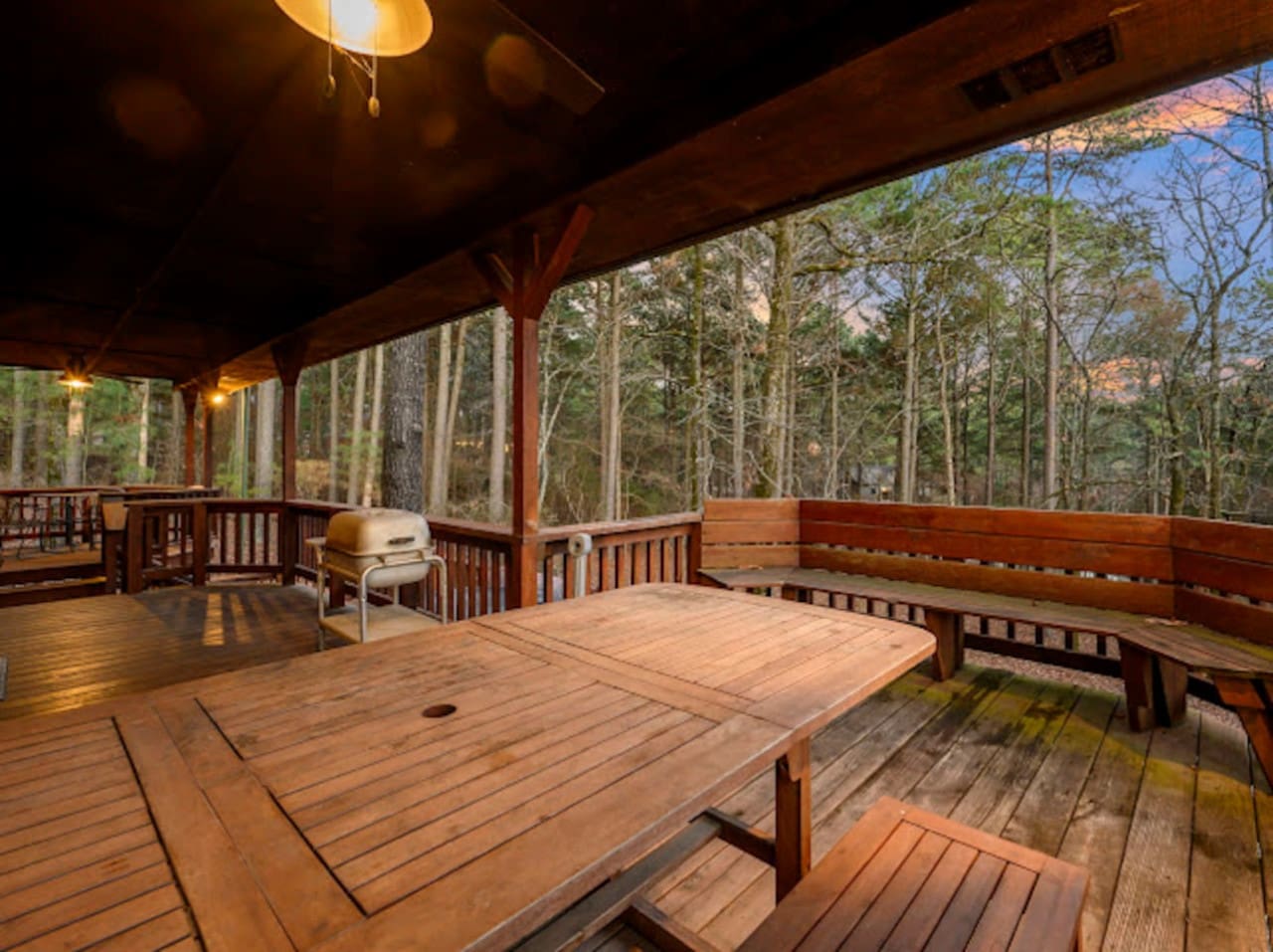 Spacious covered deck with cornhole, dining table, and stunning forest views perfect for relaxing outdoors.