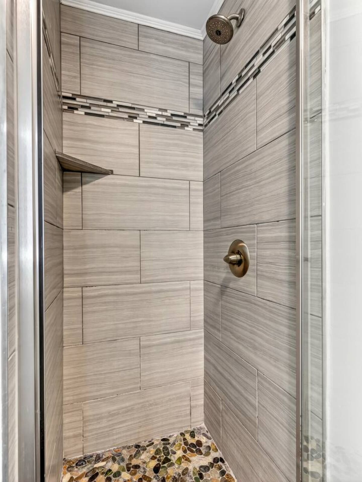 This stunning walk-in shower features sleek gray tile work, a rainfall showerhead, and a gorgeous pebble stone floor.