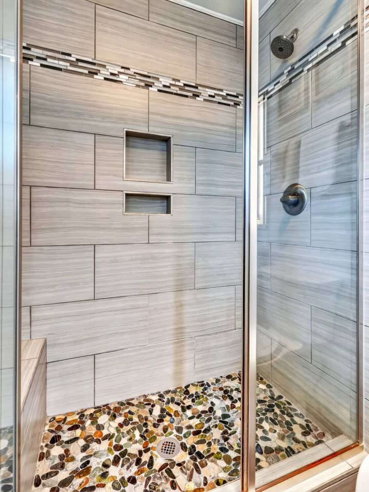 This spa-like shower features sleek wood-look tile, built-in niches, and a gorgeous river rock floor.