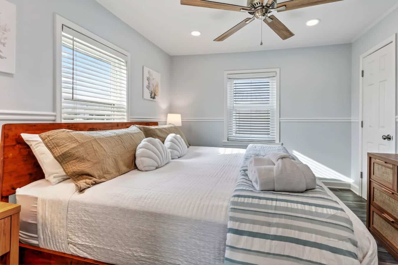 This bright, airy master bedroom features a wood bed frame, ceiling fan, and French doors that flood the space with natural light.