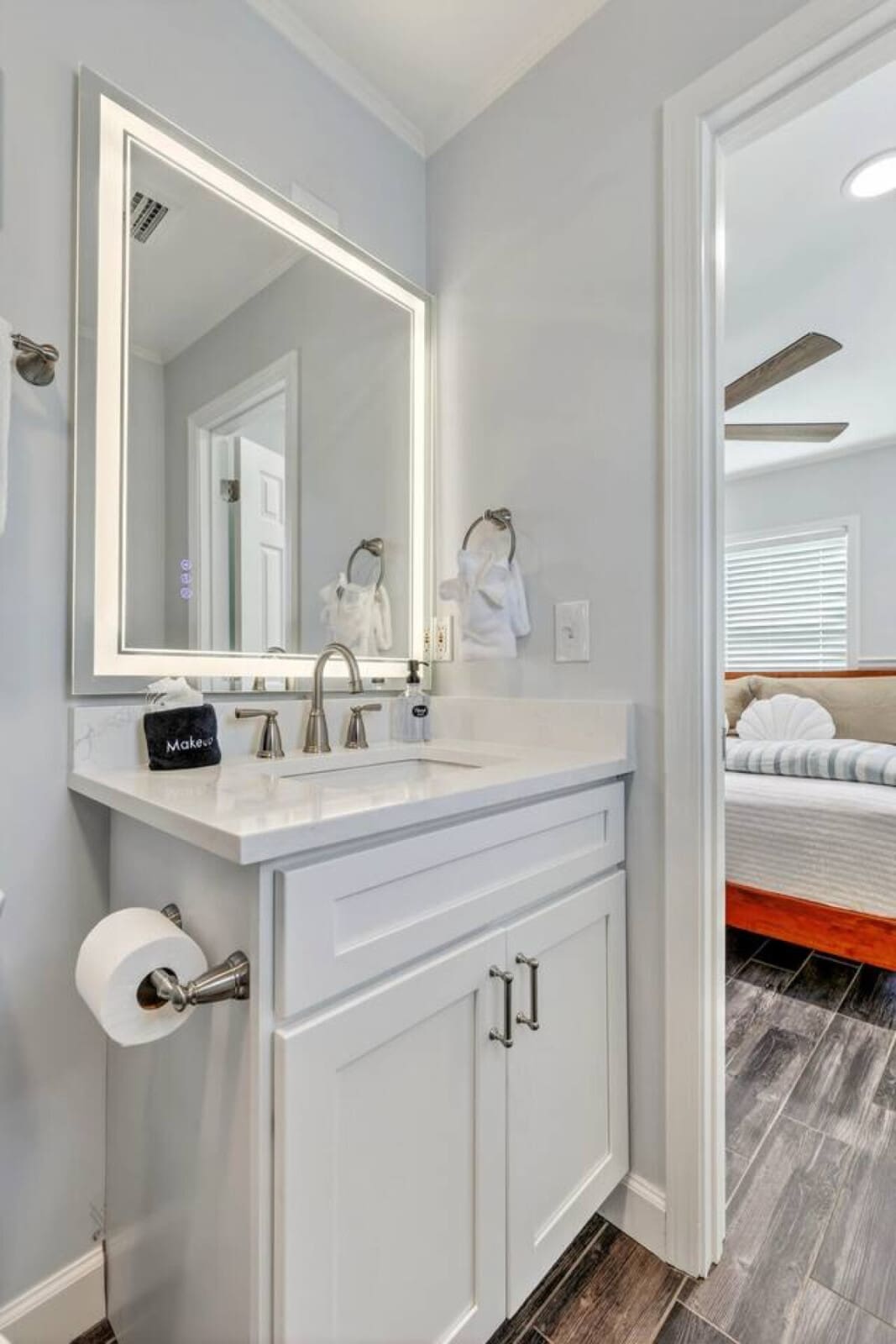 This stylish ensuite bathroom features a lighted vanity mirror and pristine white cabinetry with marble countertops.