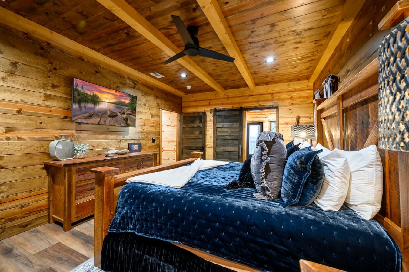 This cozy log cabin bedroom features exposed beam ceilings, a king bed, and modern amenities tucked into rustic charm.