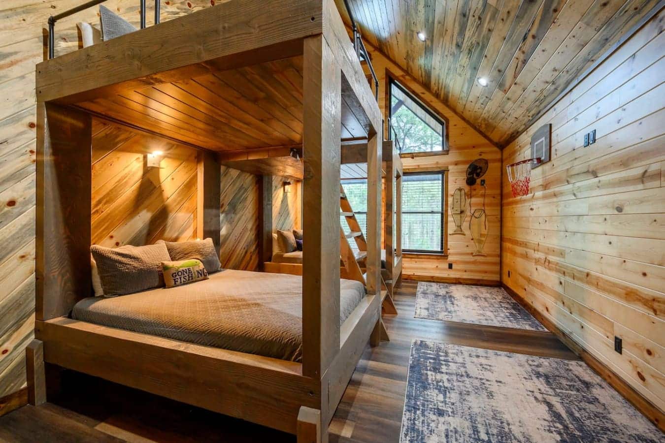 This cozy wood cabin bedroom features a custom canopy bed with warm lighting and plenty of windows flooding the space with natural light.