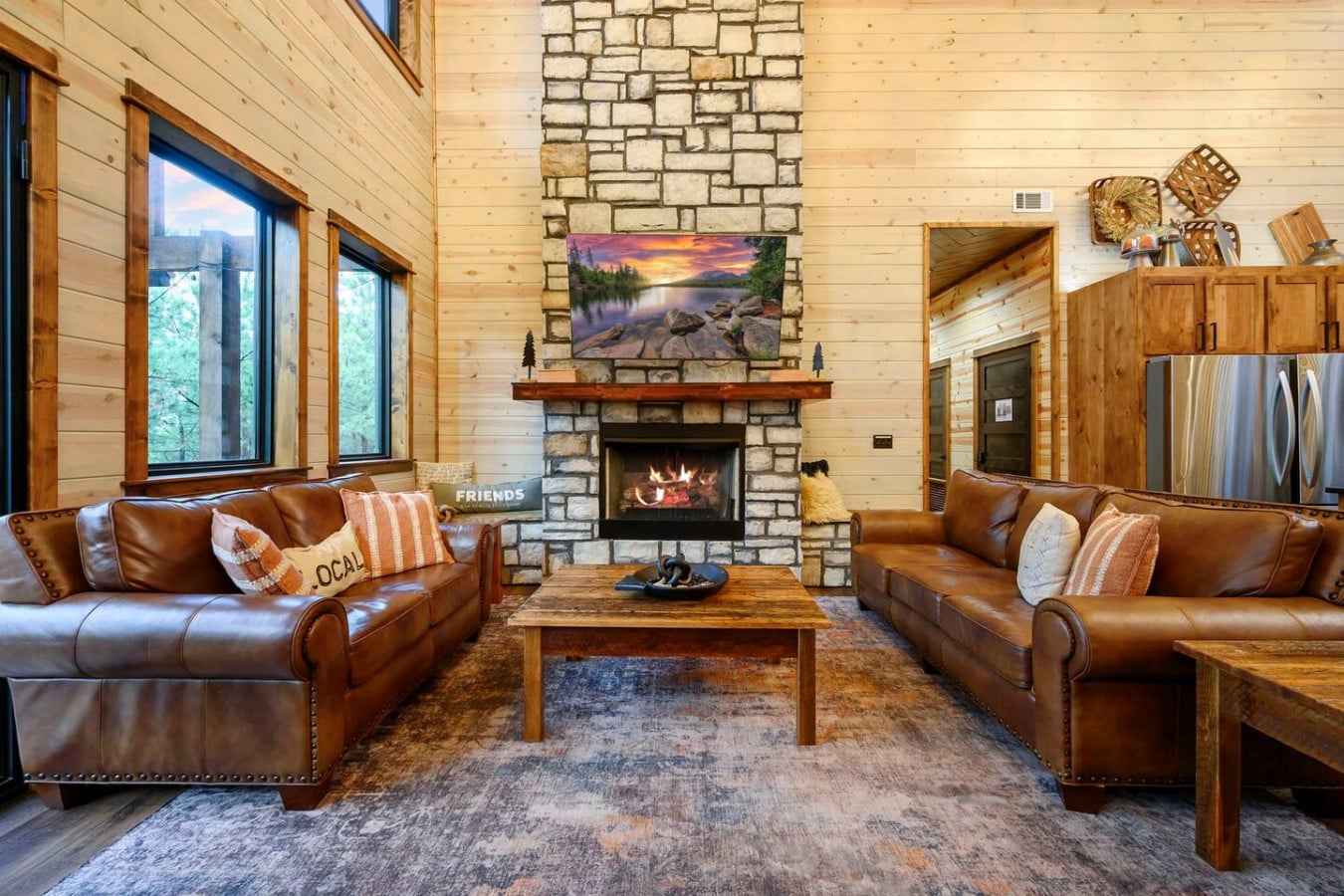 This spacious living room features a stone fireplace, cozy leather seating, and huge windows overlooking the forest.