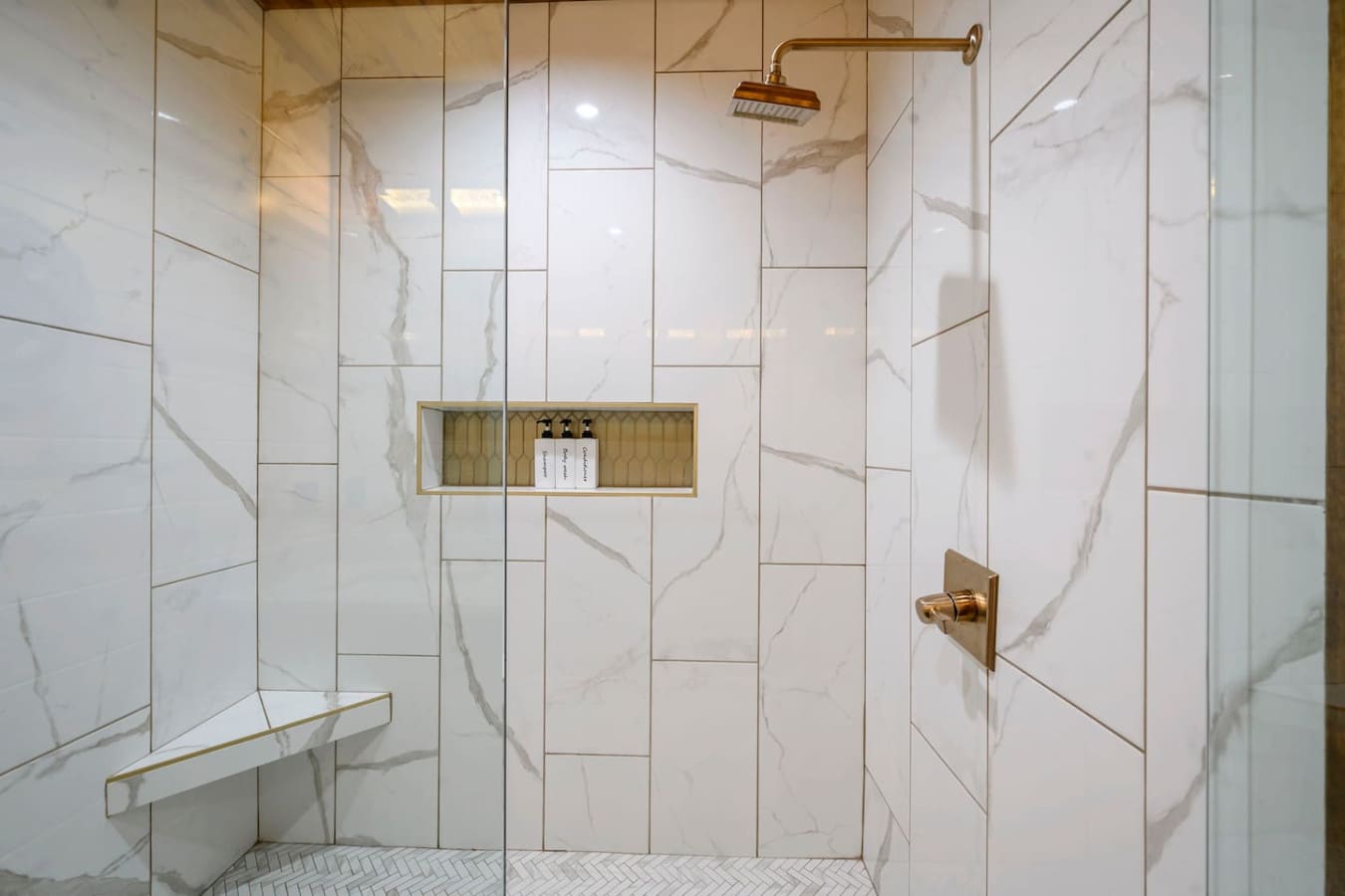 This spa-like shower features elegant marble tile, brass fixtures, and a built-in nicheu2014pure luxury.