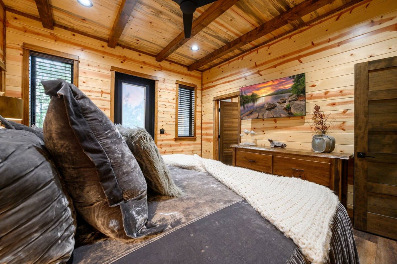 This cozy log cabin bedroom features exposed beam ceilings, rustic wood walls, and large windows with gorgeous views.