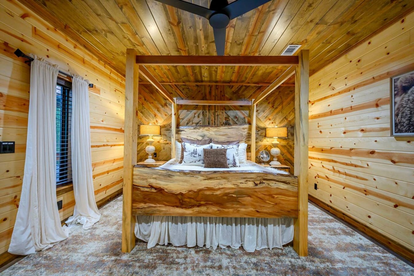 This log cabin bedroom features a stunning custom four-poster bed with vaulted wood ceilings and cozy mountain views.