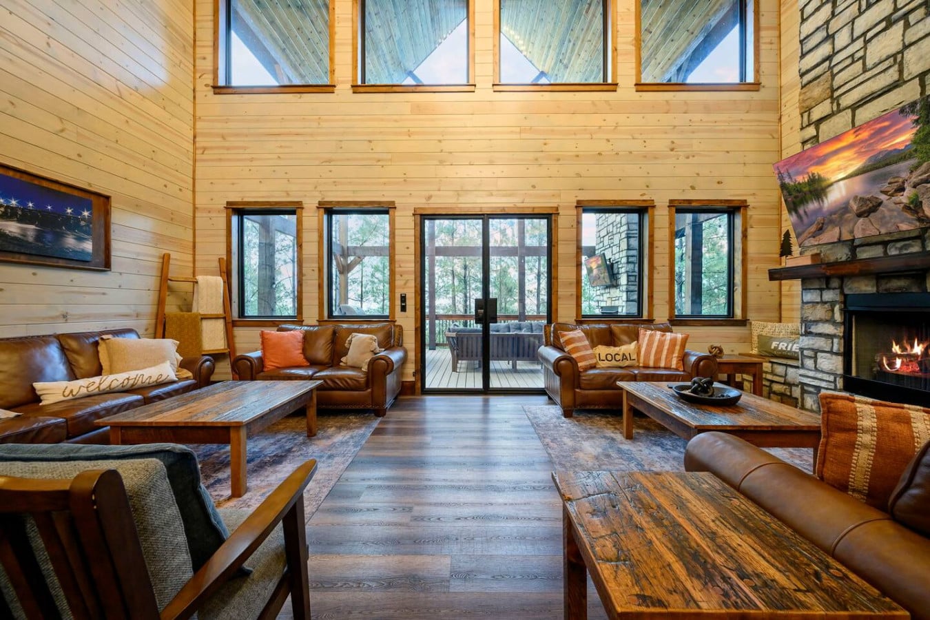 This stunning great room has soaring ceilings, a stone fireplace, and walls of windows overlooking the forest.