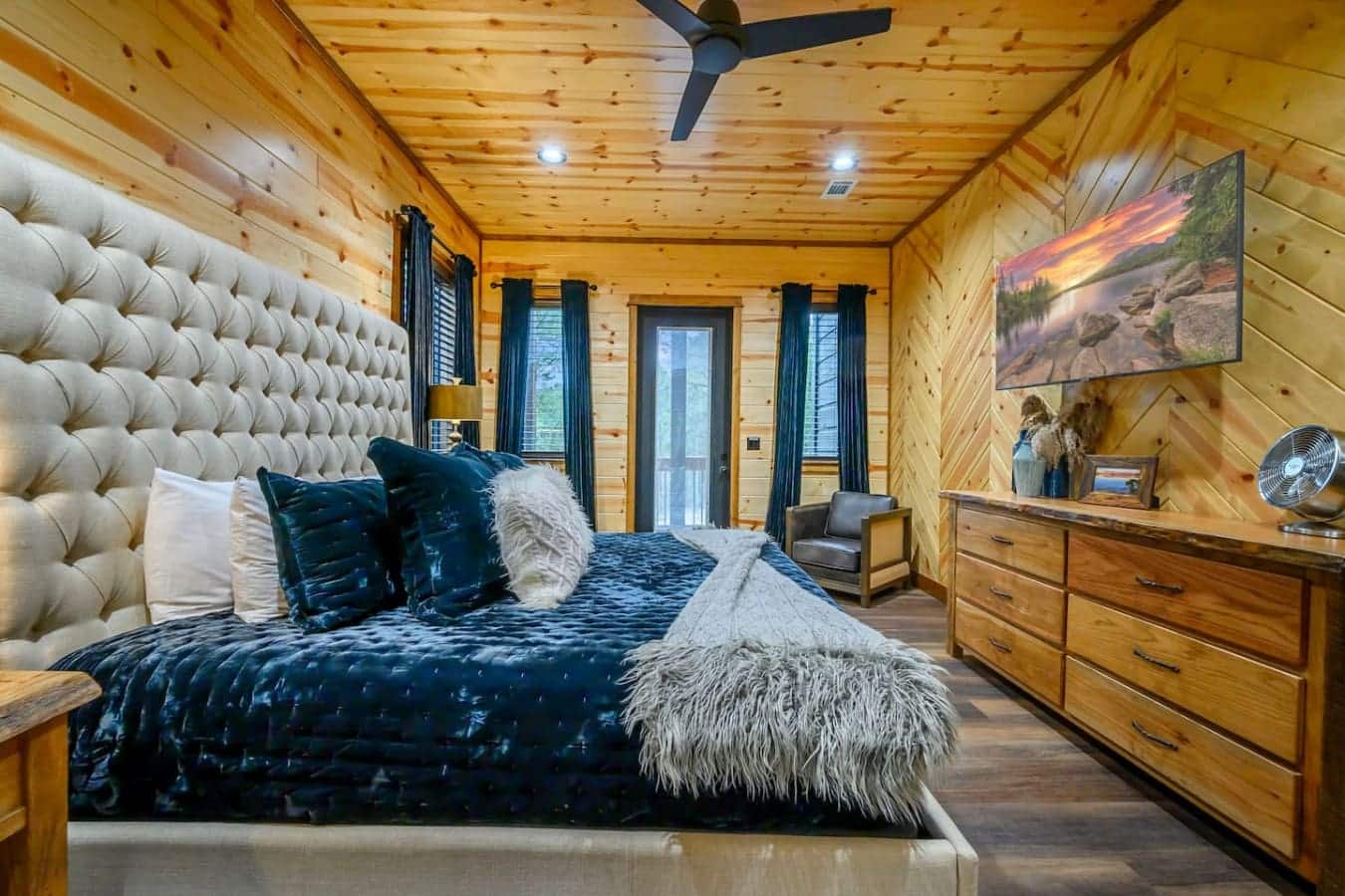 This stunning master suite features knotty pine walls, a tufted upholstered headboard, and direct access to the deck.