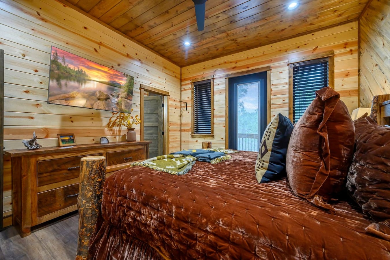 This cozy log cabin bedroom features warm wood throughout, a king bed, and those big windows bringing in tons of natural light.