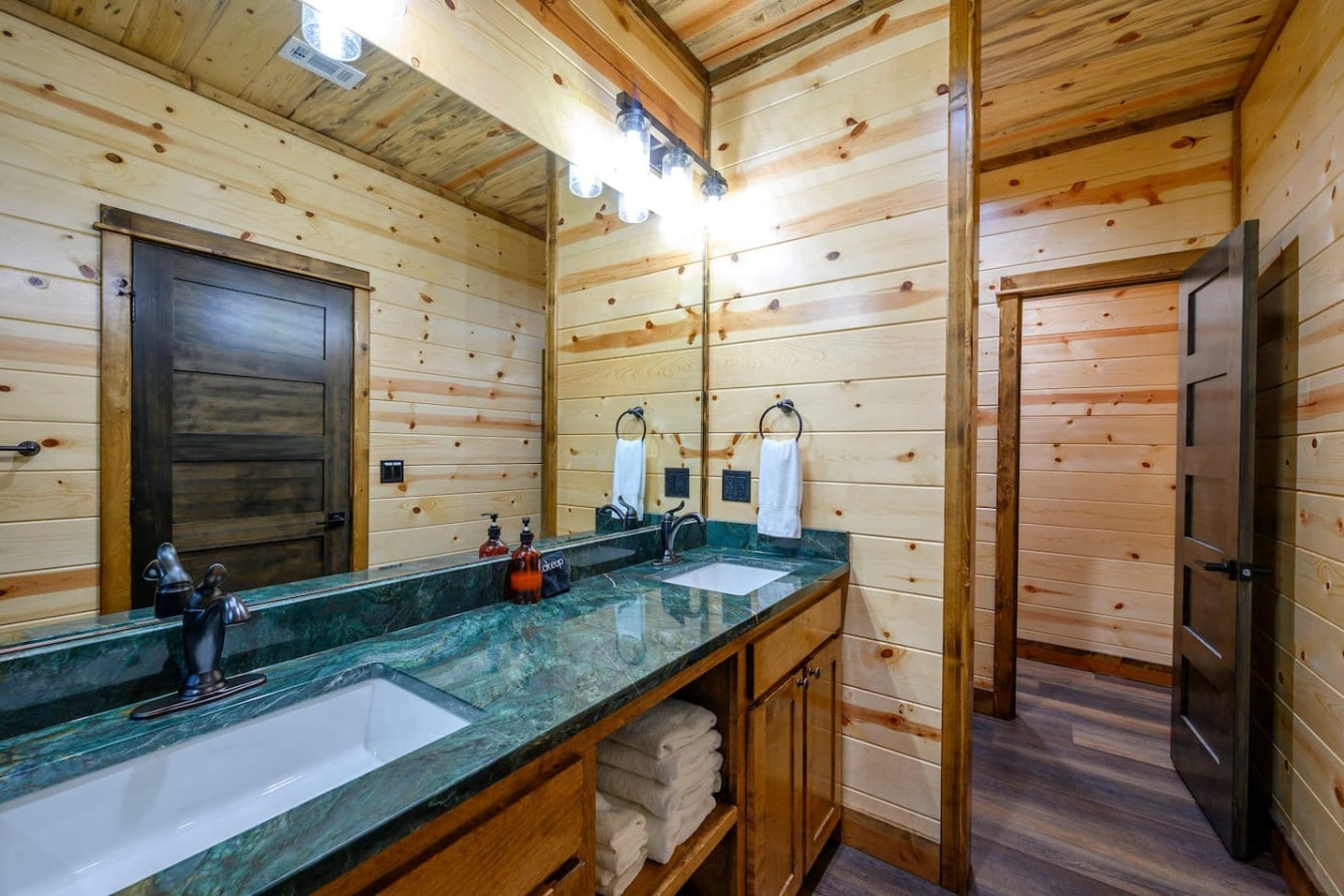This spacious log cabin bathroom features a stunning dual vanity with green marble countertops and custom wood finishes throughout.